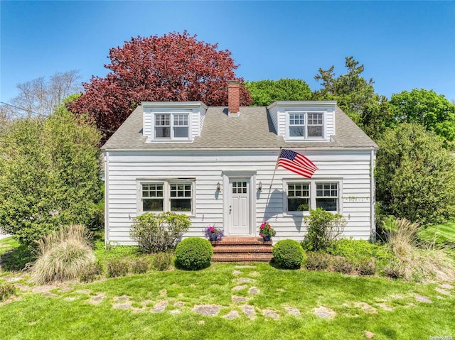 view of front of home with entry steps, a front lawn, a chimney, and a shingled roof