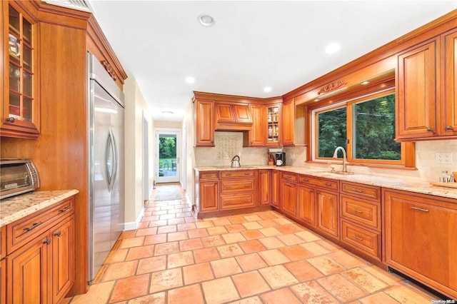 kitchen featuring sink, backsplash, light stone countertops, and built in fridge