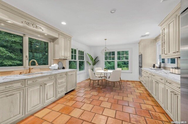 kitchen featuring sink, hanging light fixtures, oven, light stone countertops, and cream cabinetry