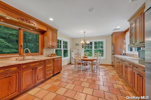 kitchen with sink, light stone countertops, decorative light fixtures, oven, and a chandelier