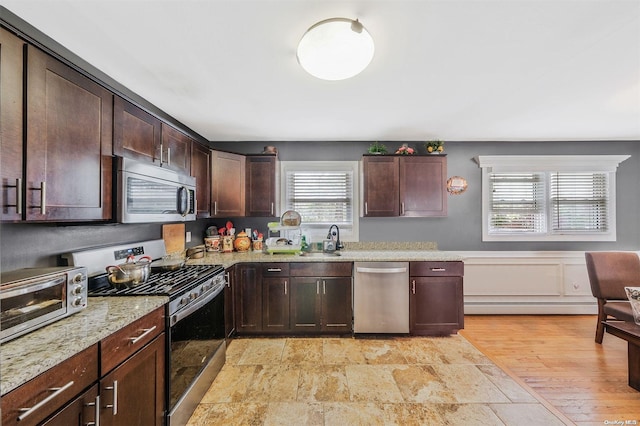 kitchen featuring appliances with stainless steel finishes, a baseboard heating unit, light stone counters, and dark brown cabinets