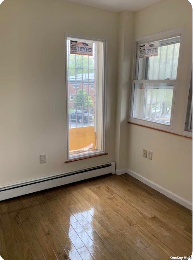 unfurnished room featuring baseboard heating, a healthy amount of sunlight, and light wood-type flooring