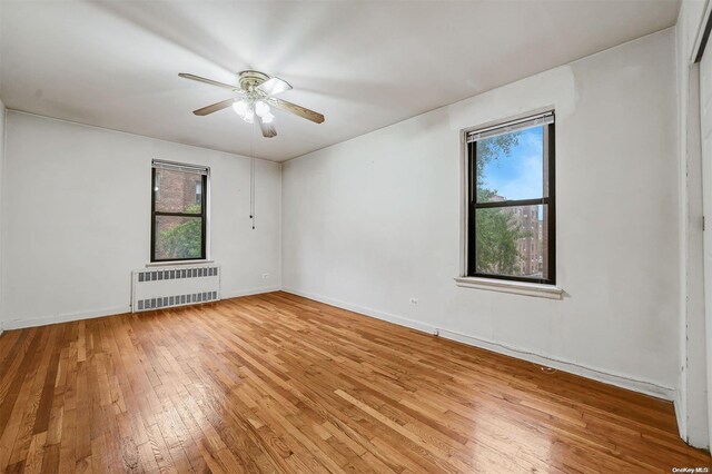 unfurnished room with radiator, a wealth of natural light, hardwood / wood-style floors, and ceiling fan