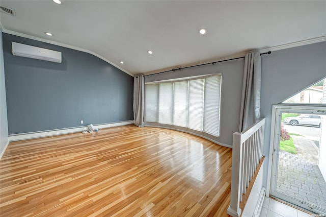 empty room featuring lofted ceiling, light wood-type flooring, crown molding, and a wall unit AC