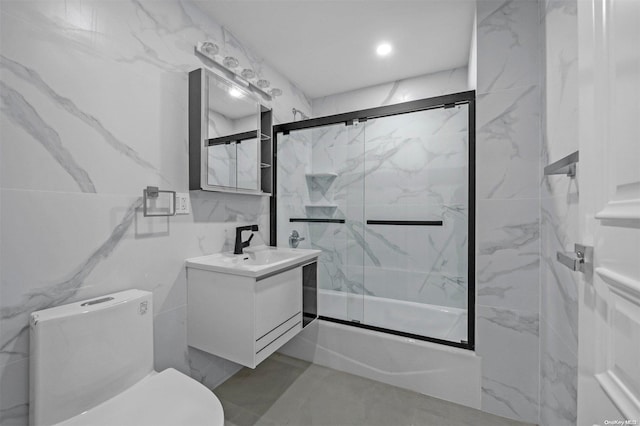 full bathroom featuring vanity, toilet, bath / shower combo with glass door, and tile walls