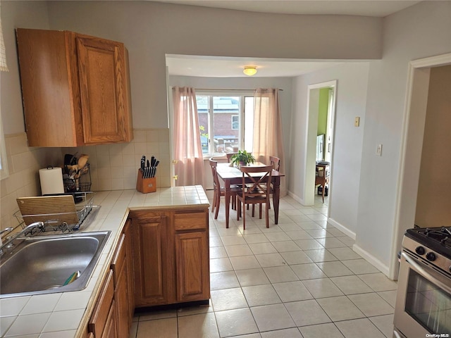 kitchen with sink, stainless steel gas range, tile countertops, decorative backsplash, and light tile patterned flooring