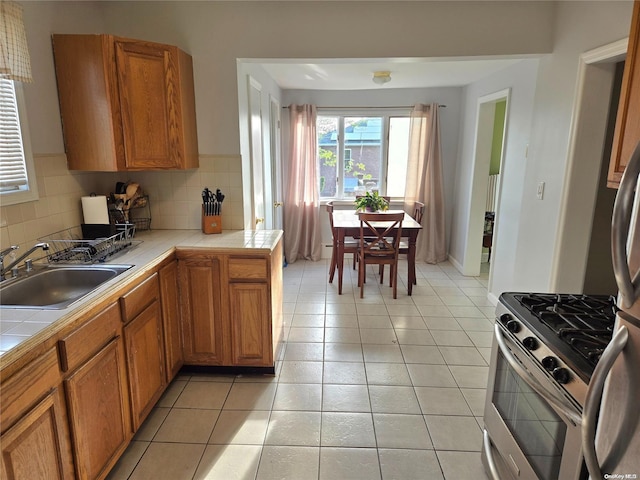 kitchen featuring tile counters, decorative backsplash, sink, and gas range