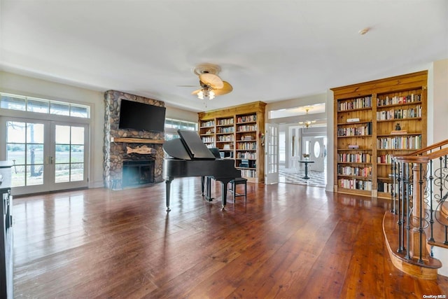 misc room featuring wood-type flooring, french doors, a stone fireplace, and ceiling fan