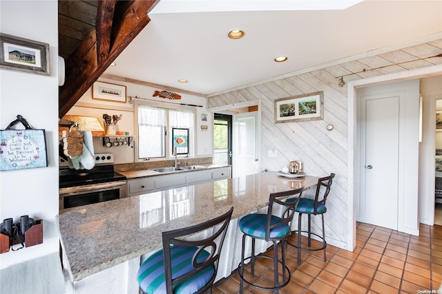 kitchen featuring sink, light tile patterned floors, a kitchen breakfast bar, light stone counters, and stainless steel range with electric cooktop