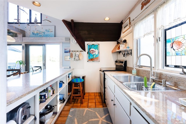 kitchen featuring stainless steel range with electric stovetop, white cabinets, dark tile patterned floors, and sink