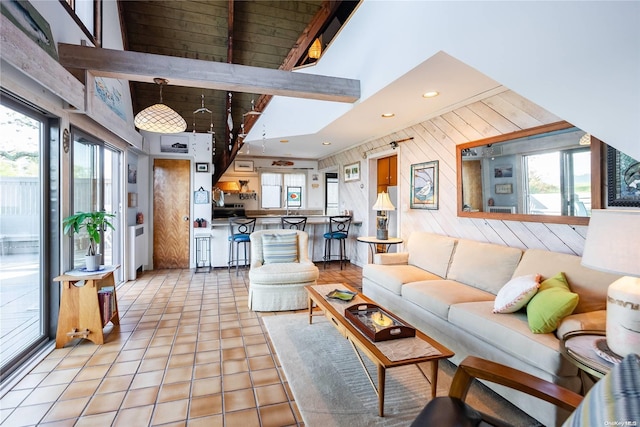 living room with a wealth of natural light, light tile patterned floors, lofted ceiling with beams, and wood walls