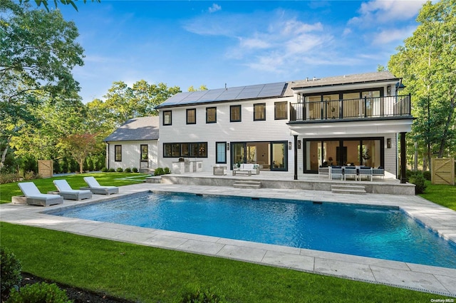 rear view of property featuring solar panels, a balcony, an outdoor living space, a patio area, and a lawn