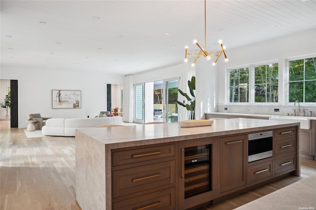 kitchen with stainless steel oven, decorative backsplash, decorative light fixtures, light hardwood / wood-style floors, and beverage cooler