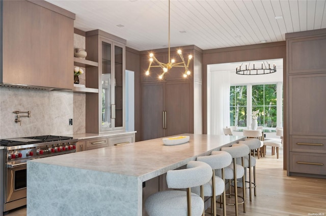 kitchen featuring a center island, designer stove, pendant lighting, light hardwood / wood-style floors, and decorative backsplash