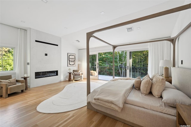 bedroom featuring access to outside, a large fireplace, light hardwood / wood-style floors, and lofted ceiling