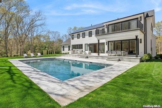 rear view of property with a yard, a patio area, a balcony, and solar panels