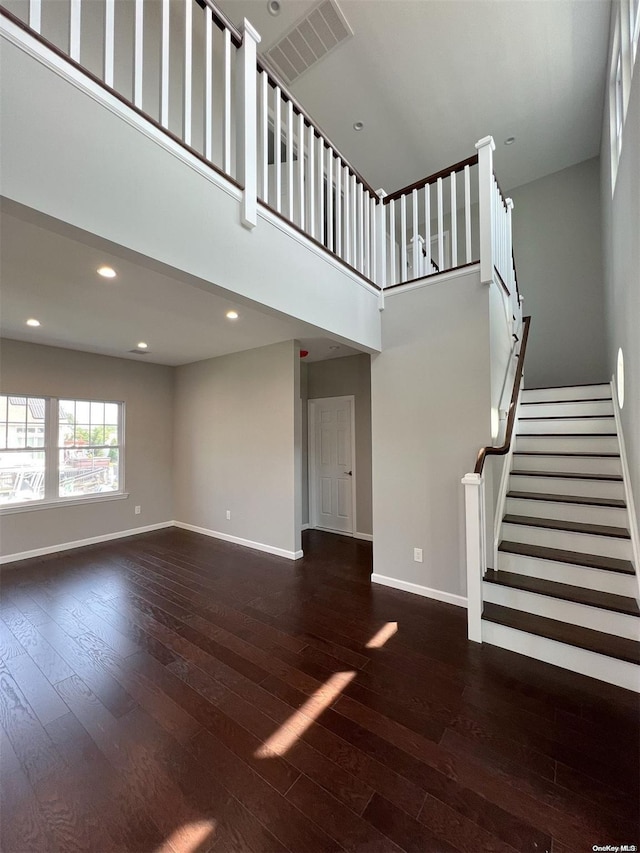 unfurnished living room featuring a towering ceiling and dark hardwood / wood-style flooring