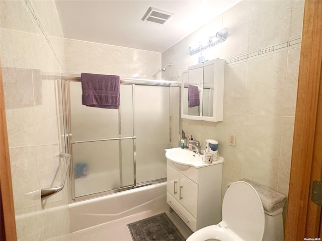 full bathroom featuring shower / bath combination with glass door, vanity, toilet, and tile walls