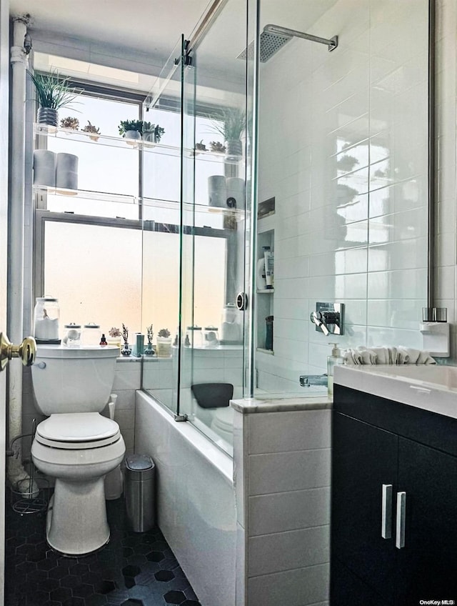 full bathroom featuring combined bath / shower with glass door, vanity, tile walls, tile patterned flooring, and toilet