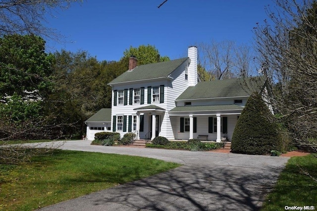 colonial home with covered porch, a garage, and a front lawn