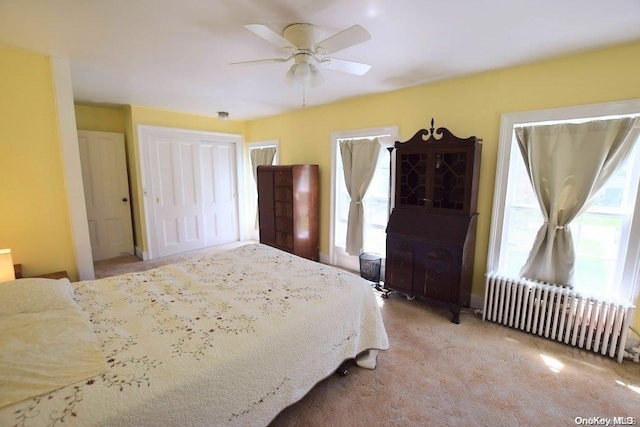 bedroom featuring light carpet, a closet, radiator, and ceiling fan