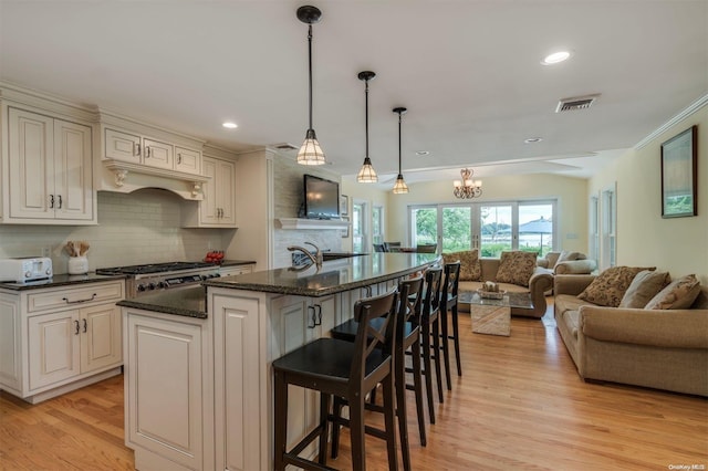 kitchen featuring an inviting chandelier, a center island with sink, hanging light fixtures, tasteful backsplash, and light hardwood / wood-style floors