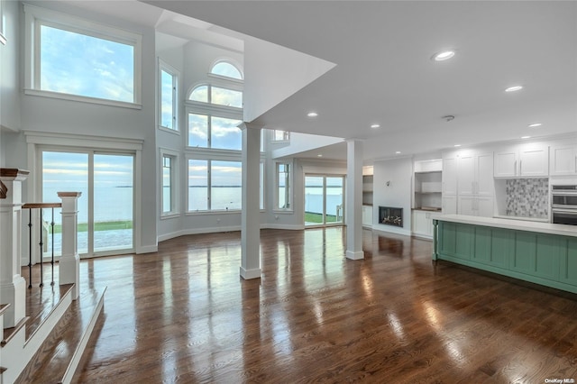 unfurnished living room with a towering ceiling, a water view, a healthy amount of sunlight, and dark hardwood / wood-style floors