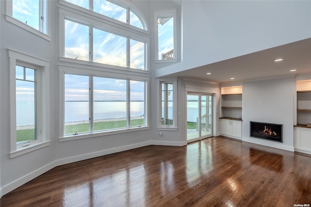 unfurnished living room with a water view, a healthy amount of sunlight, and a high ceiling