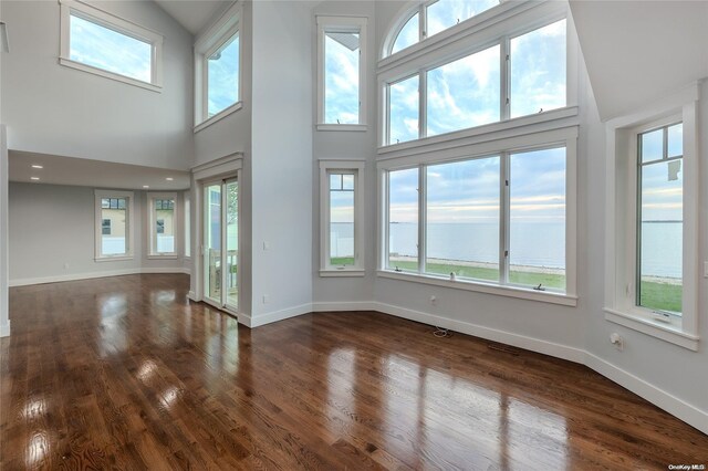 unfurnished living room with a water view, dark wood-type flooring, and a high ceiling