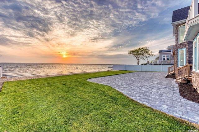 yard at dusk featuring a water view, a patio, and a view of the beach