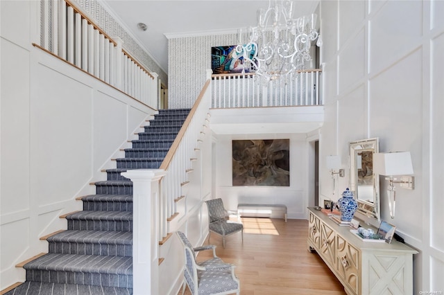 staircase featuring wood-type flooring, an inviting chandelier, and ornamental molding