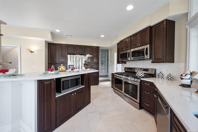 kitchen featuring tasteful backsplash, light stone counters, dark brown cabinets, and appliances with stainless steel finishes