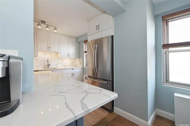 kitchen featuring white cabinetry, light stone countertops, tasteful backsplash, stainless steel fridge, and hardwood / wood-style flooring