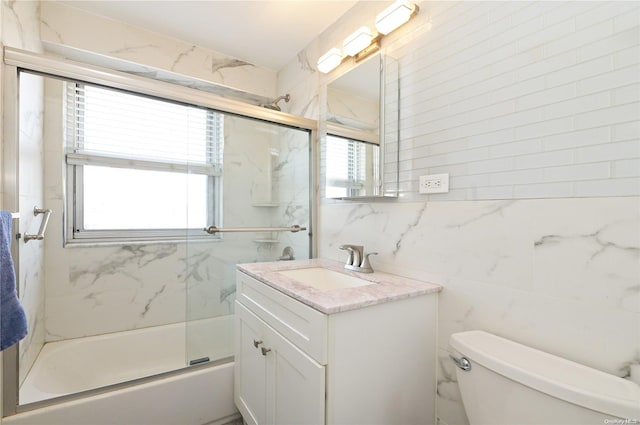 full bathroom featuring vanity, toilet, bath / shower combo with glass door, and tile walls