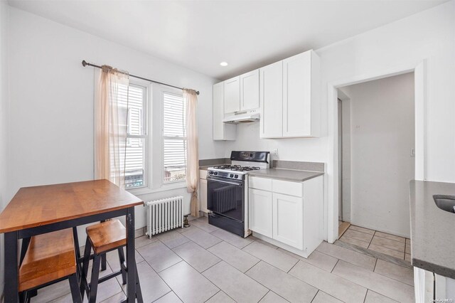 kitchen with white cabinets, light tile patterned flooring, radiator heating unit, and black range with gas cooktop