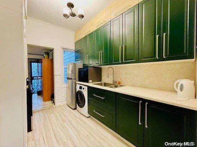 kitchen with light wood-type flooring, stainless steel appliances, sink, green cabinetry, and washer / dryer