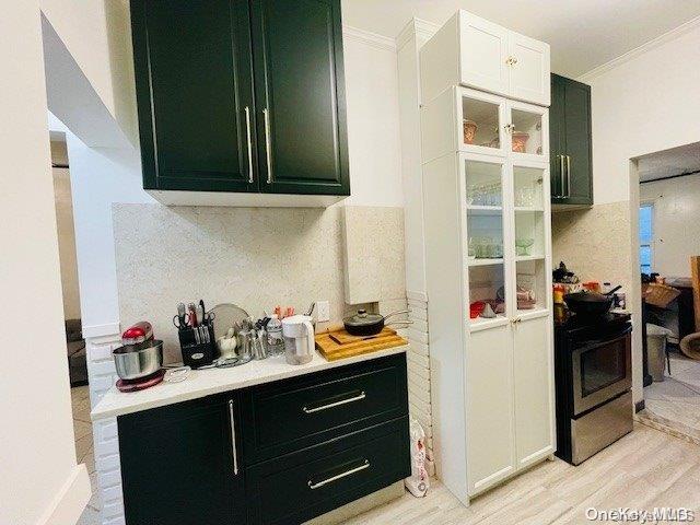 kitchen with backsplash, ornamental molding, light hardwood / wood-style flooring, white cabinetry, and black / electric stove