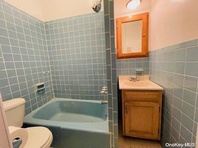 full bathroom featuring vanity, toilet, tile walls, and tiled shower / bath combo