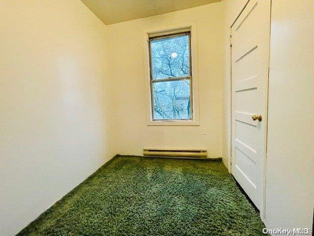 carpeted spare room with a baseboard heating unit