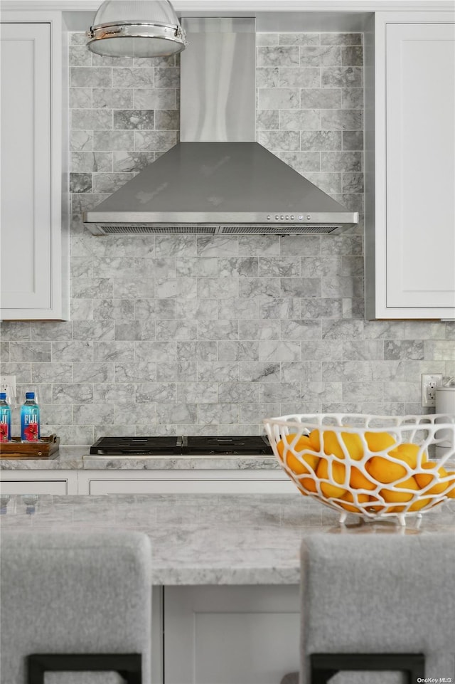 kitchen featuring decorative backsplash, gas stovetop, white cabinetry, and wall chimney range hood