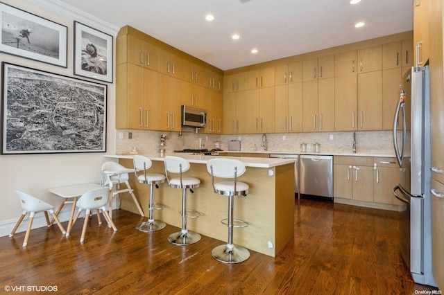 kitchen featuring kitchen peninsula, decorative backsplash, dark hardwood / wood-style flooring, stainless steel appliances, and a breakfast bar area