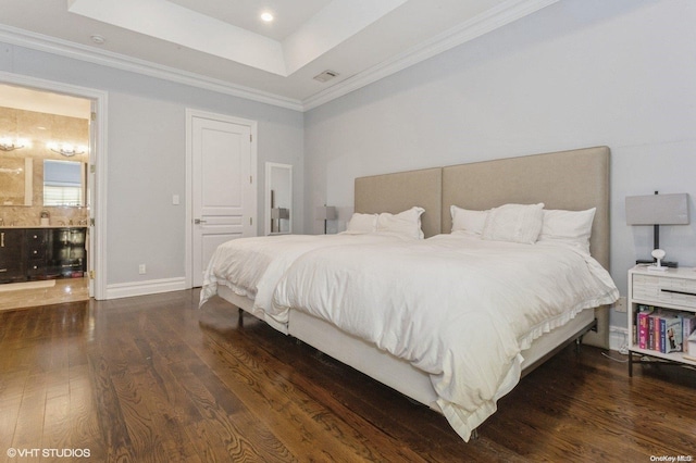 bedroom with a tray ceiling, connected bathroom, crown molding, and dark hardwood / wood-style floors