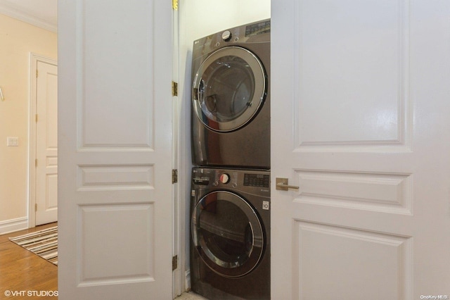 clothes washing area with wood-type flooring, stacked washing maching and dryer, and ornamental molding