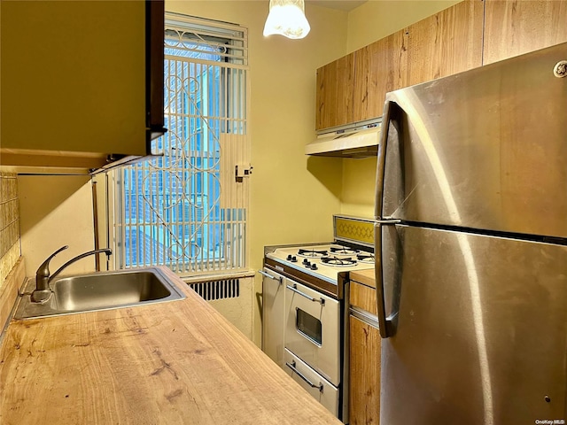 kitchen with stove, sink, butcher block countertops, stainless steel refrigerator, and hanging light fixtures