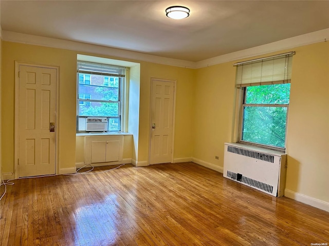 empty room with cooling unit, light wood-type flooring, radiator heating unit, and crown molding