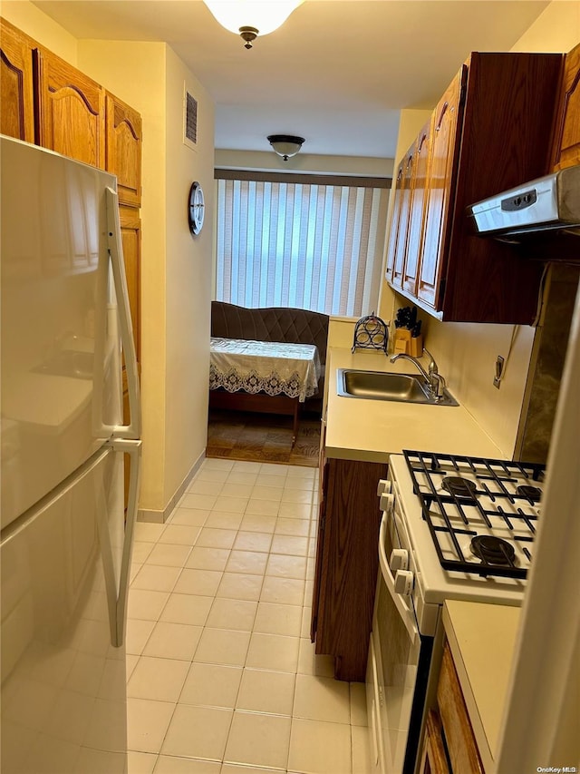 kitchen featuring refrigerator, gas range gas stove, extractor fan, sink, and light tile patterned floors