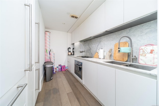 kitchen featuring stainless steel oven, sink, gas cooktop, white cabinets, and light wood-type flooring