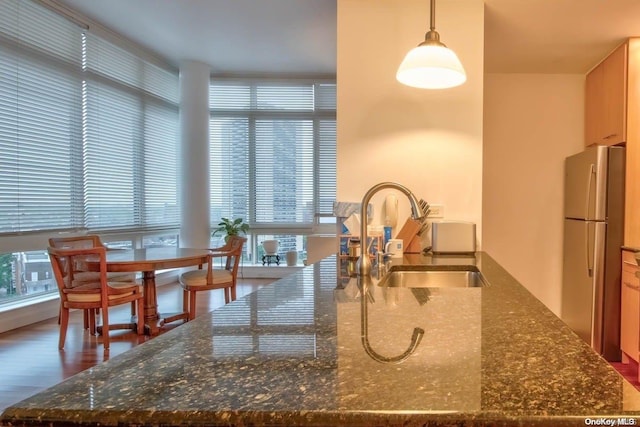 kitchen with stainless steel fridge, dark wood-type flooring, sink, pendant lighting, and dark stone countertops