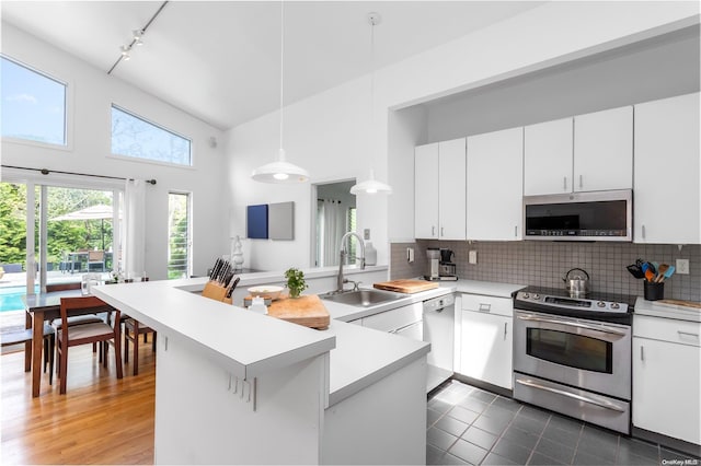 kitchen featuring kitchen peninsula, stainless steel appliances, high vaulted ceiling, white cabinets, and hanging light fixtures