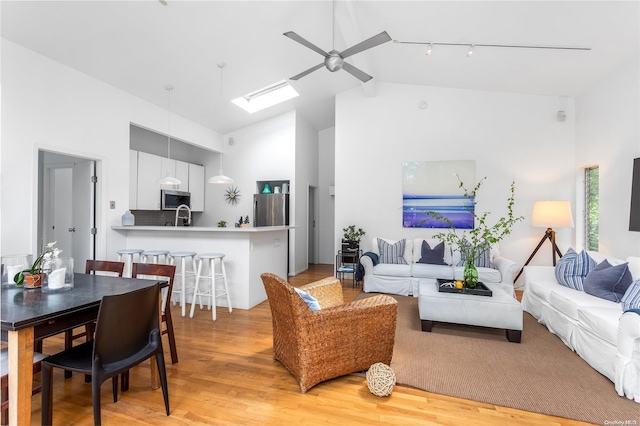 living room with light wood-type flooring, a skylight, ceiling fan, sink, and high vaulted ceiling